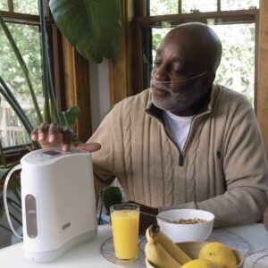 Man uses Oxlife Liberty Portable Oxygen Concentrator while sitting at table for breakfast
