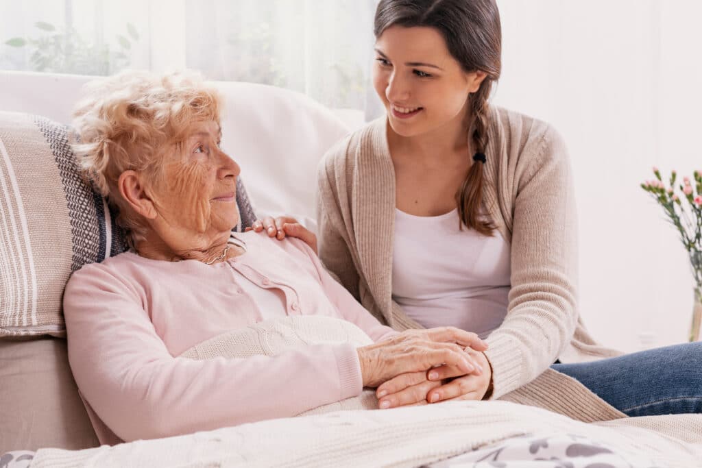 elderly woman sits with caregiver on hospital bed from you can