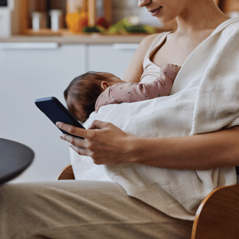 Mother holding newborn while researching best breast pumps on her phone