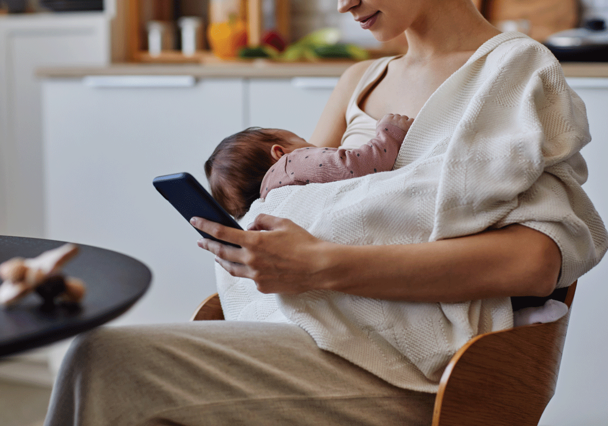 Mother holding newborn while researching best breast pumps on her phone