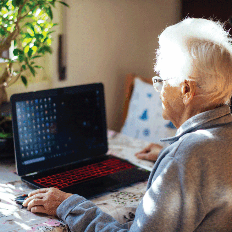 Senior traveler sitting at a table using a laptop, preparing a checklist for traveling with oxygen on an airplane.