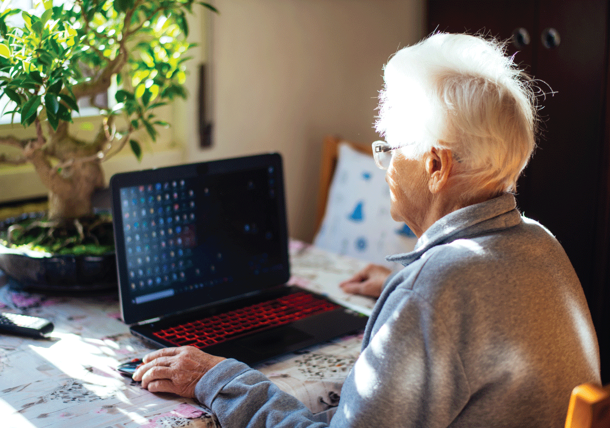 Senior traveler sitting at a table using a laptop, preparing a checklist for traveling with oxygen on an airplane.