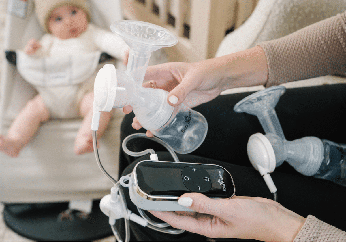 A parent holding a small electric breast pump with their child in the background